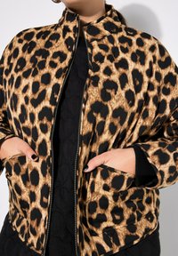 Giacca bomber trapuntata con un motivo leopardato in marrone e nero, dotata di zip anteriore e tasche laterali. Tessuto testurizzato, colletto alto.