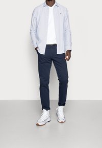 Jasnoniebieska koszula w paski z długim rękawem na białej koszulce, do tego granatowe chinosy i białe wysokie trampki z gumowymi podeszwami.