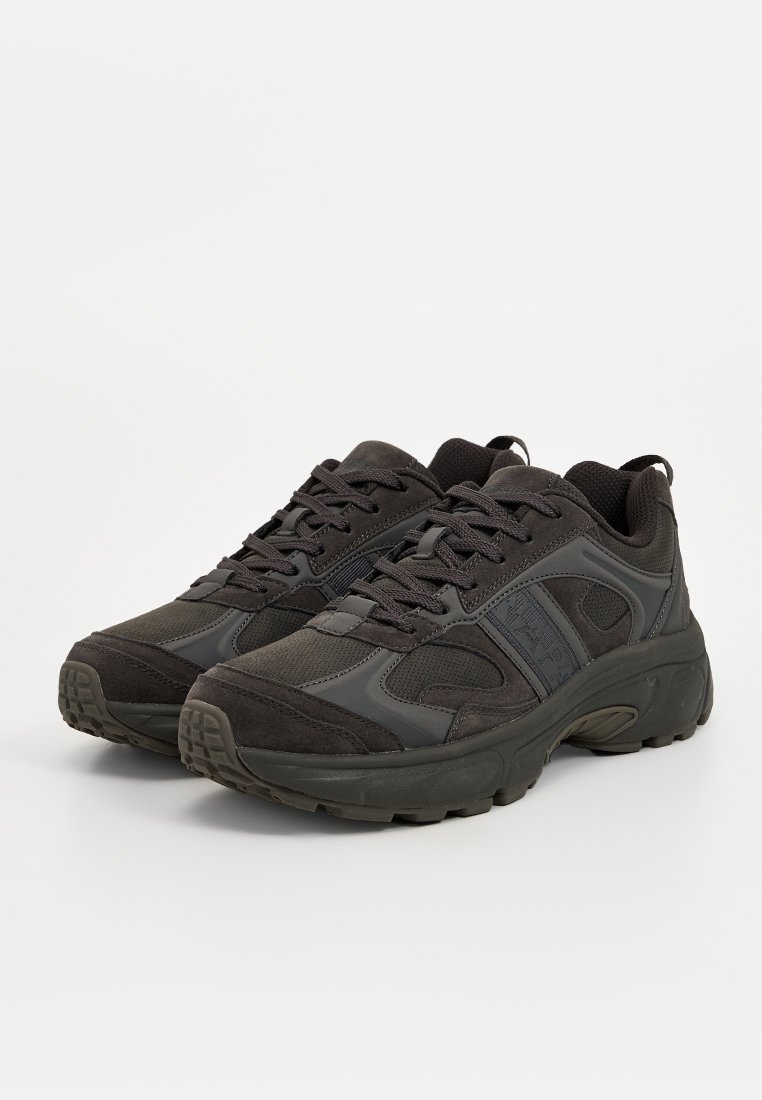 Zapatillas deportivas negras que combinan materiales de ante y malla, con forma redondeada, suelas de goma gruesas y detalles texturizados en los laterales.