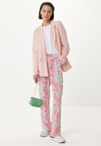 Różowa lniana marynarka, biała koszulka, kolorowe spodnie we wzory kwiatowe w odcieniach różu i zieleni, zielona torebka i białe trampki.