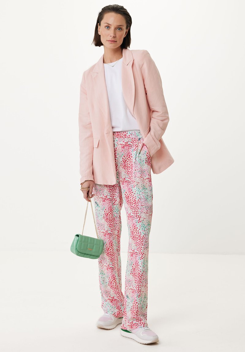 Różowa lniana marynarka, biała koszulka, kolorowe spodnie we wzory kwiatowe w odcieniach różu i zieleni, zielona torebka i białe trampki.