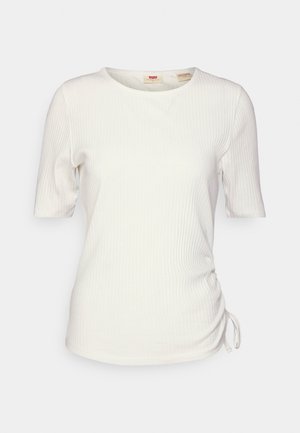 Balta ribota T-kreklu ar īsām piedurknēm un apaļu kakla izgriezumu. Iezīmē pielāgojamu sānu drapējumu ar aukliņu detaļu. Mīksta auduma tekstūra.