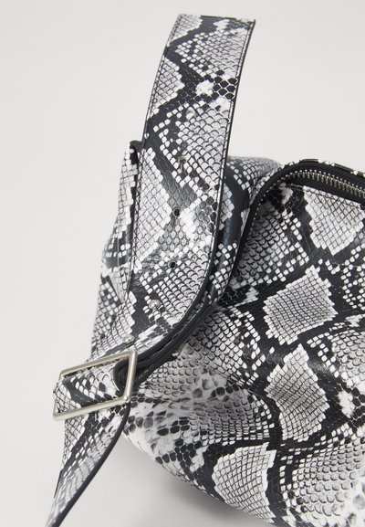 Sac imprimé serpent noir et blanc avec une surface lisse et texturée. Dispose d'une large bandoulière avec une boucle en argent et d'une fermeture éclair.