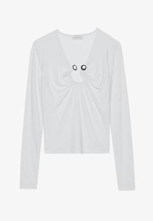 Biely dlhý rukáv top s hlbokým výstrihom do V, zdobený nariasenou látkou okolo výstrihu a dvomi čiernymi kruhovými akcentmi.