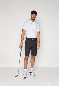 Biela polo košeľa s golierom a logom, čierne šortky, čierny opasok a biele golfové topánky. Prilba a golfová palica dotvárajú vzhľad.