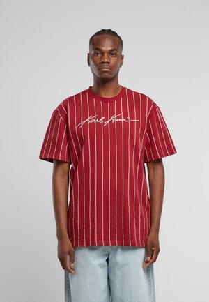 Bordeaux gestreiftes T-Shirt mit weißen vertikalen Linien und Logo-Stickerei. Kurze Ärmel, runder Ausschnitt, lockere Passform. Denim-Shorts sind sichtbar.