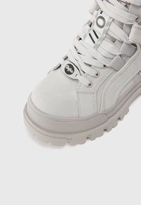 Valkoiset sneakerit, joissa on teksturoitu nahkainen yläosa, pyöreä varvas ja paksu kumipohja. Varustettu hopeisella logolla, valkoisilla nauhoilla ja raidallisilla yksityiskohdilla.