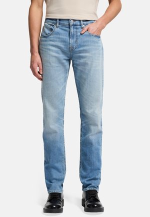 Jeans in denim blu chiaro con una vestibilità dritta, design a cinque tasche, leggere sfumature e dettagli in ottone. Indossati con scarpe nere stringate.