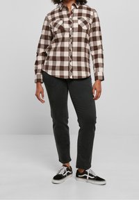 Camicia a scacchi marrone e crema con colletto a bottone, due tasche sul petto e maniche lunghe, abbinata a jeans neri e sneakers nere.