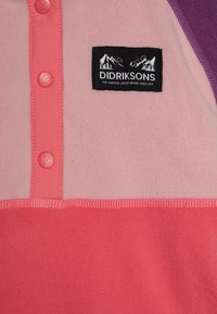 Pullover in pile nei colori rosa e corallo con un accento viola, chiusura a bottoni e un'etichetta nera con grafiche di montagne.