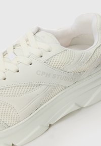 Hvite joggesko med mesh- og skinndesign, teksturerte aksenter og en tykk såle. Gravet logo med teksten "CPH STUDIOS."
