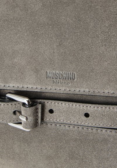 Γκρι υλικό από σουέντ με ανάγλυφο λογότυπο Moschino Milano και σουέντ ζώνη που ασφαλίζει με ασημένια μεταλλική αγκράφα.