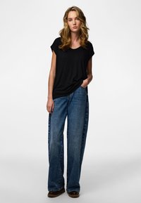 Fekete, rövid ujjú póló laza szabású, világos koptatott farmernadrággal párosítva. A ruházat laza sziluettet és finom textúrát mutat.