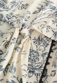 Cream fabric with black floral print tied in a knot and a vertical black lace trim along one edge.