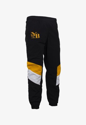 Zwarte sportbroek met gele en witte geometrische accenten, elastische tailleband en omgeslagen enkels. Heeft een logo aan de bovenkant links.