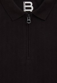 Schwarzes Polo mit Reißverschluss aus strukturiertem Stoff, mit geripptem Kragen und einem kleinen Logotag in der Nähe des Ausschnitts.