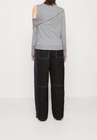 Haut gris à manches longues avec un design unique dans le dos. Associé à un pantalon large noir avec des coutures blanches et de grandes poches.