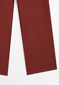Pantalon large couleur rouille avec un tissu lisse et texturé et des ourlets propres et droits. Pas de poches visibles ni d'éléments métalliques.