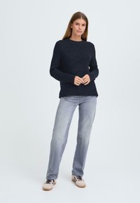 Pull à côtes bleu marine avec des manches longues, associé à un jean gris délavé et des baskets de couleur claire. Design simple et texturé avec un col rond.