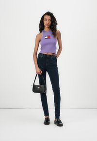 Lavendel ribbet crop top med logo-patch, mørke skinny jeans og en liten svart håndveske. Modellen har på seg svarte loafers og står på en lys bakgrunn.