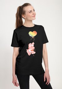 Černé tričko s růžovým medvídkem, který drží duhový balón ve tvaru srdce, se soft-touch texturou a uvolněným střihem.