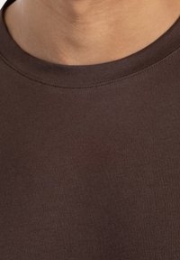 Camiseta de cuello redondo marrón, hecha de algodón suave con una textura lisa y detalles de costura sutiles a lo largo del escote.