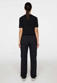 Czarny t-shirt z krótkim rękawem i czarne spodnie cargo. Strój ma luźny krój, a spodnie posiadają kieszenie oraz gładką teksturę.