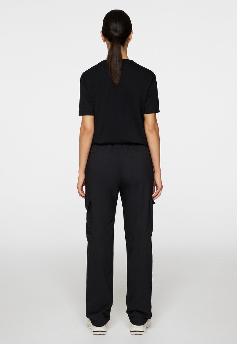 T-shirt nera a maniche corte e pantaloni cargo neri. L'outfit ha una vestibilità rilassata con tasche sui pantaloni e una texture liscia.