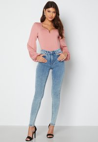 Långärmad rosa bodysuit med V-ringning och puffärmar, i kombination med högmidjade ljusblå skinny jeans och svarta högklackade skor.