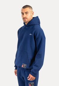 Felpa blu navy realizzata in tessuto misto cotone, con tasca a marsupio frontale e ricamo del logo. Include etichette a contrasto vicino all'orlo.