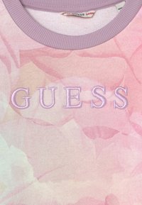 Lyserød tie-dye sweatshirt med broderet "GUESS" tekst i lysere pink. Glat stof med en lavendel ribbet halsudskæring.