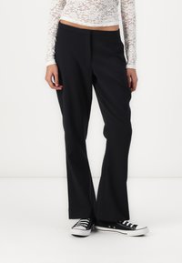 Pantalons noirs ajustés avec un design à jambe droite, fabriqués en tissu léger. Portés avec un top en dentelle blanche et des sneakers noires.