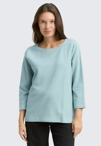 Hellblaues Longsleeve-Shirt mit Rundhalsausschnitt und strukturiertem Stoff, kombiniert mit schwarzen Hosen. Einfaches, lässiges Design ohne Verzierungen.