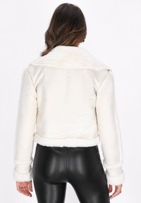 Afgekorte cr�èmekleurige nepfur jas met grote kraag en witte nepshearling manchetten. Soepele textuur en naadloos achterdesign, gecombineerd met zwarte leggings.