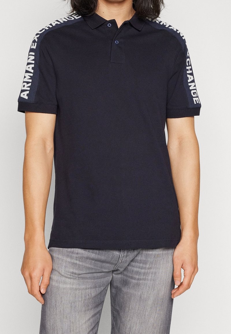 Polo bleu marine avec patte de boutonnage à deux boutons, manches courtes avec le logo blanc "ARMANI EXCHANGE" le long des épaules, en coton.