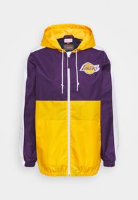 Lilla og gul lynlåsjakke med hætte, prydet med hvide detaljer og Los Angeles Lakers-logo på brystet. Letvægtsmateriale.