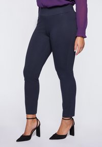 Marina leggings tillverkade av elastisk tyg med hög midja, prydda med sömdetaljer och matchade med svarta högklackade skor med ankelsnöre.