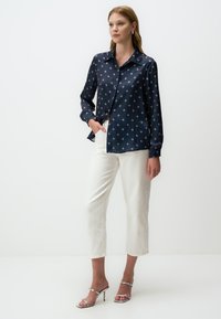 Marineblouse met wit geometrisch patroon, knoopsluiting, lange mouwen, gecombineerd met witte cropped broek en zilveren haksandalen.