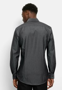 Dunkelgraues Langarm-Hemd mit Knopfleiste und strukturierter Oberfläche, spitzem Kragen und abgerundetem Saum; mit Knöpfen an den Manschetten und Rückenschlitzen.