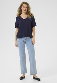 Top de manga corta azul marino con escote en V, corte relajado, combinado con jeans de pierna recta azul claro y zapatos planos negros. Textura de tela suave.