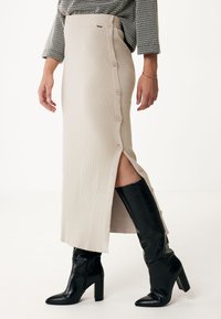 Stickad beige midikjol med sidoknäppning och hög slits, tillsammans med svarta ankel- och knähöga klackstövlar.