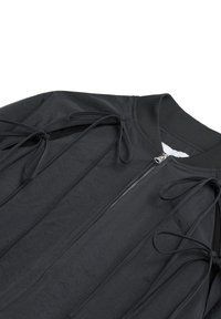 Chaqueta bomber negra con tejido texturizado, cremallera frontal y lazos ajustables a ambos lados para estilo y ajuste.
