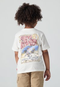 Balta medvilnė marškinėliai su spalvinga grafika nugarinėje pusėje, kurioje pavaizduota "Levi Strauss & Co." ir kaubojaus scena, trumpomis rankovėmis ir laisvu siluetu.