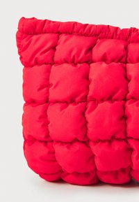 Borsa tote rossa soffice con costruzione in nylon trapuntato, sezioni quadrate distintive e bordo superiore arricciato. Texture liscia con pochi accessori.