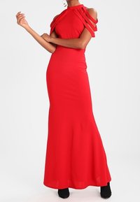 Abito lungo rosso aderente con scollo all'americana e spalle scoperte. Il tessuto è liscio e il design presenta spalline drappeggiate.