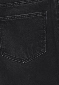 Černá džínová tkanina s viditelnou zadní kapsou, která má dvojité prošívání. Hladká textura a mírně vybledlý vzhled.