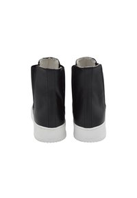 Botas de cuero negras hasta el tobillo con suelas de goma blanca, con un diseño elegante y textura suave, vista desde atrás. Costuras reforzadas visibles.