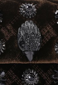 Clutch in velluto nero con ornamenti elaborati, tra cui un fermaglio metallico simile a una piuma e accenti di cristallo circolari di diverse dimensioni.