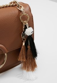 Borsa sintetica marrone con texture e accessori in oro, caratterizzata da frange multicolori in nero, marrone e bianco attaccate a un portachiavi.