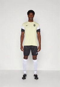 Geltoni ir juodi futbolo apranga su logotipu, trumpomis rankovėmis, juodais šortais ir baltais kojinėmis; pagaminta iš lengvos, kvėpuojančios medžiagos.